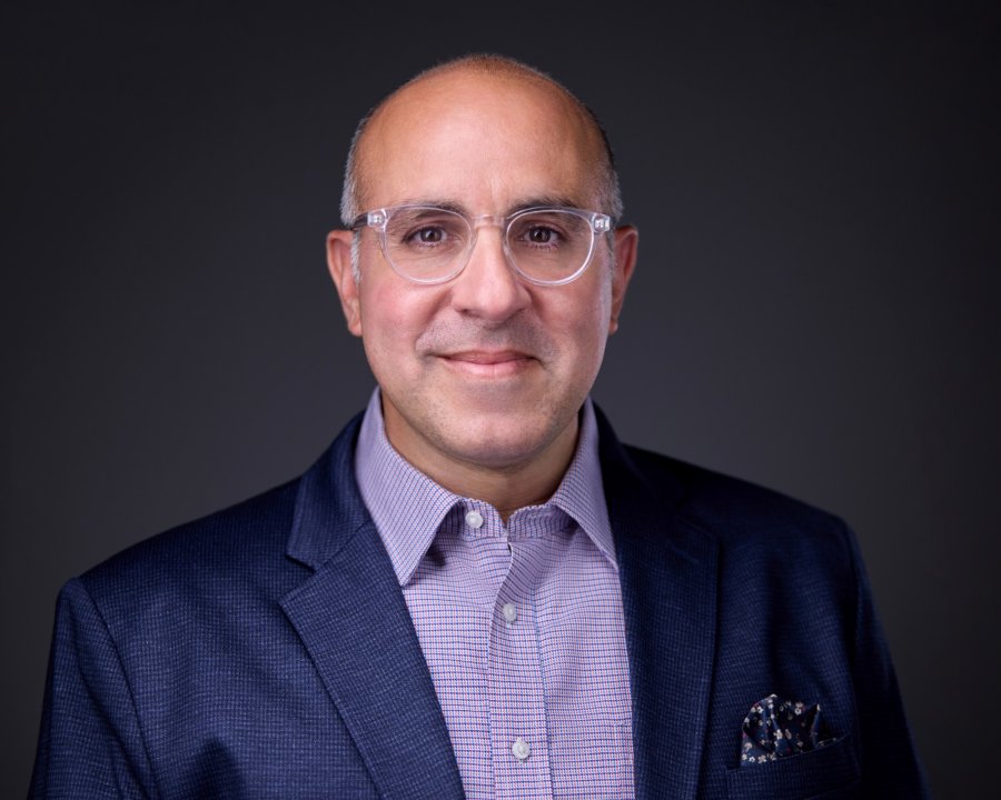 Portrait of Kerim Kfuri in a navy jacket and clear-framed glasses.