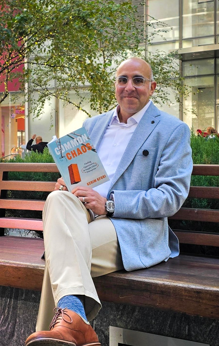 Kerim Kfuri sitting on a bench in the city, holding a copy of Common Chaos.